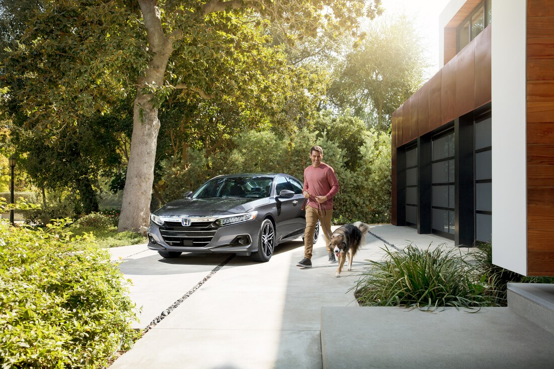 2022-Honda-AccordHybrid-Touring-Sedan-L03.png grey Honda Accord Hybrid sedan parked in front of a modern home with the driver walking a dog near it