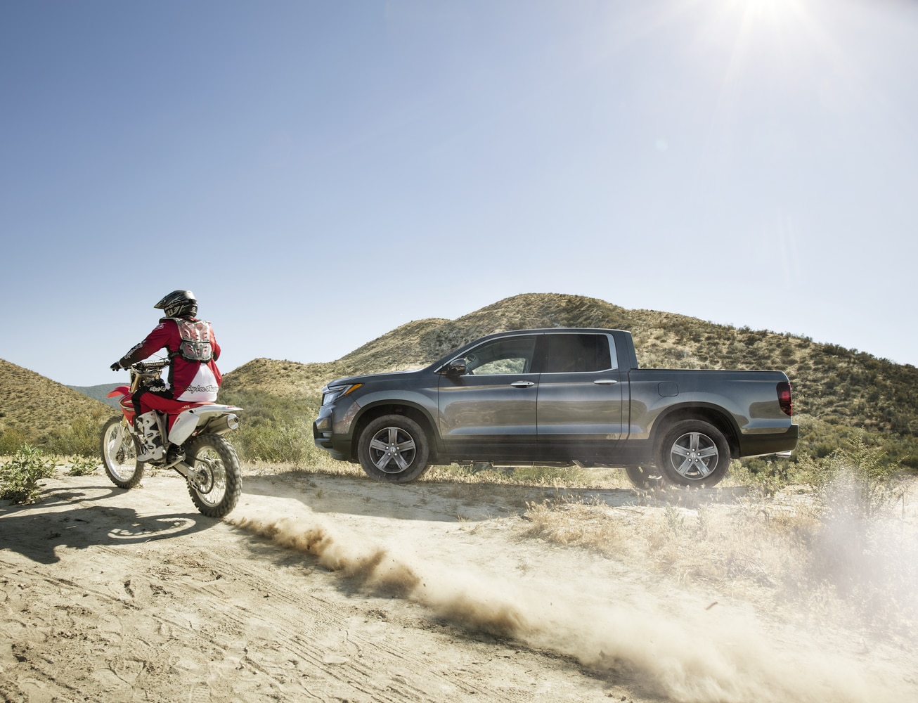 2021-Honda-Ridgeline-RTLE-Truck-L04.png silver Honda Ridgeline truck parked on a desert dune with a motor bike driving by