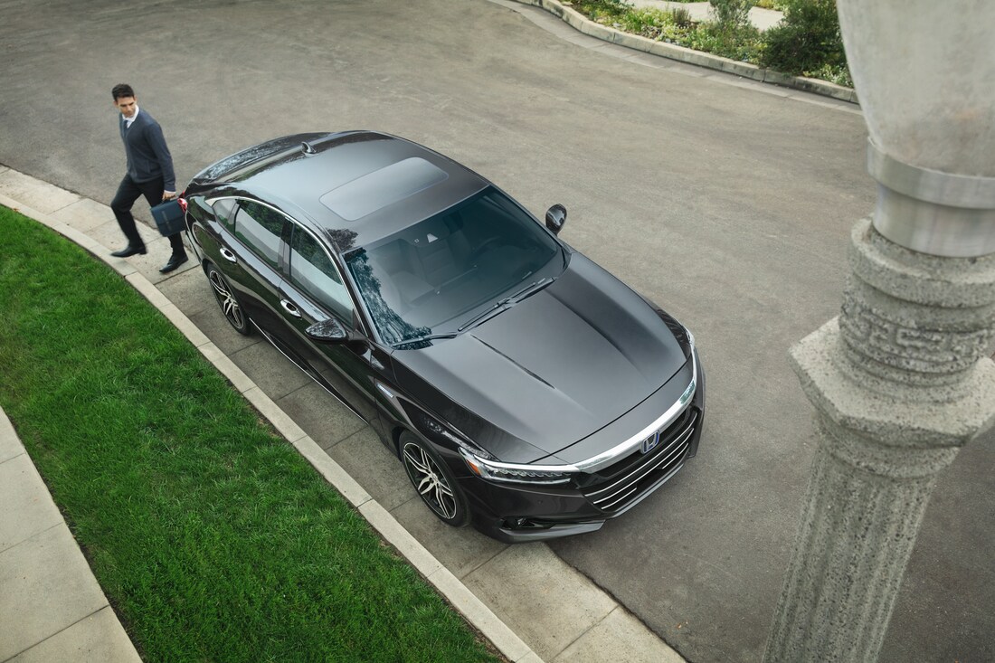 2022-Honda-AccordHybrid-Touring-Sedan-L02.png aerial drone shot of a dark grey Honda Accord hybrid sedan with the driver walking behind it with a briefcase