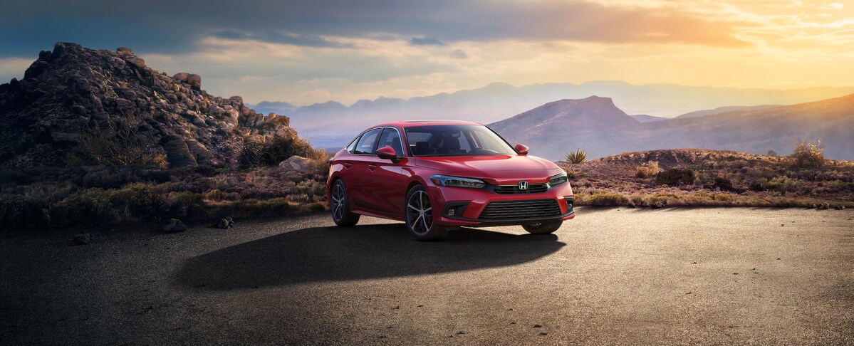 2022-Honda-Civic-Touring-Sedan-L02 (2).png red Honda Civic sedan parked on an empty lot in front of a large boulder
