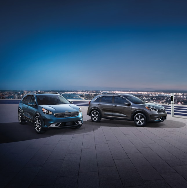2022-KIA-NiroPlugIn-Lineup-L01.png blue and green Kia Niro Plug-In hybrids parked at rooftop charging stations