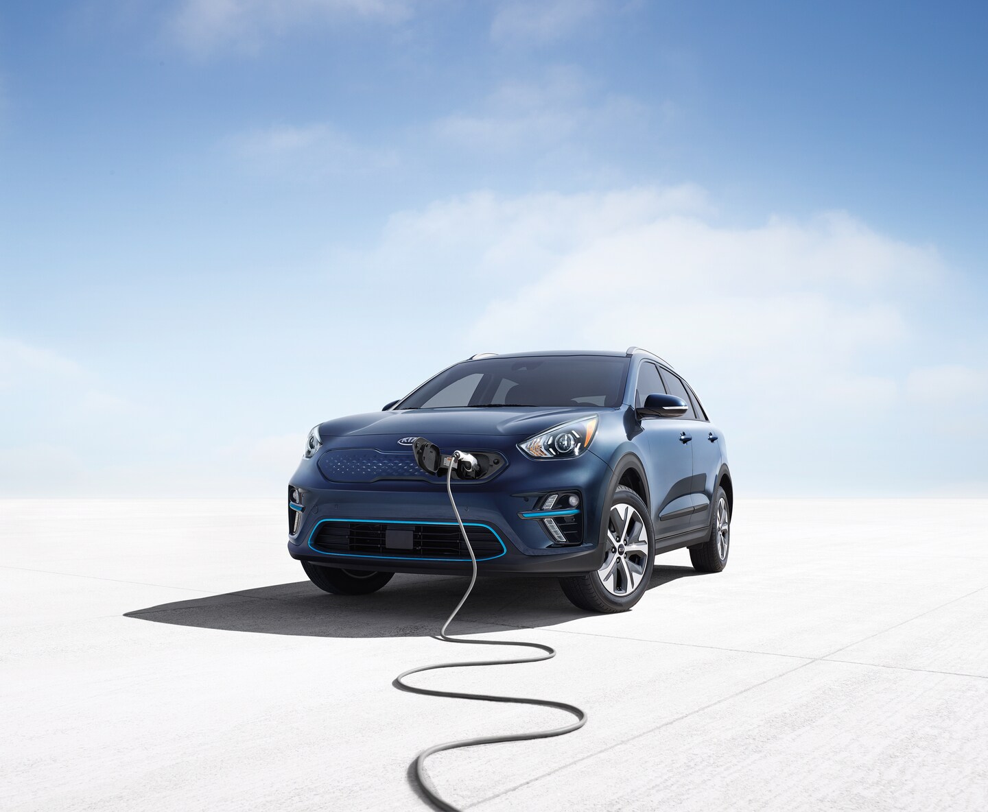blue Kia Niro EV plugged into a charger with a blue sky and cloud background
