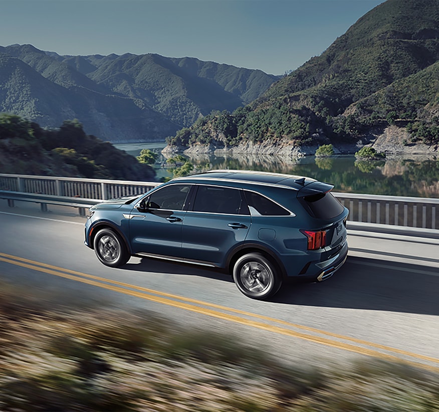 2024-KIA-Sorento-EXHybrid-SUV.png Kia Sorento Hybrid SUV driving on a bridge near a waterway with scrub brush hills