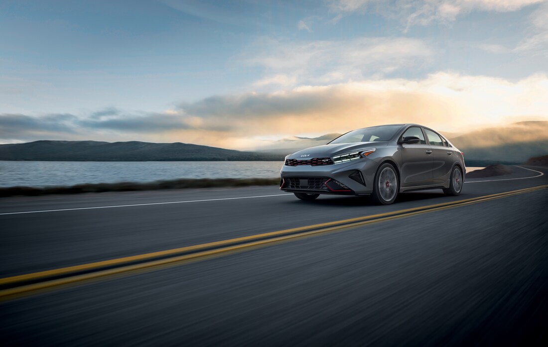 2023-KIA-Forte-GT-GT2Package-Sedan-L06.png silver Kia Forte sedan with red trim, driving next to the water