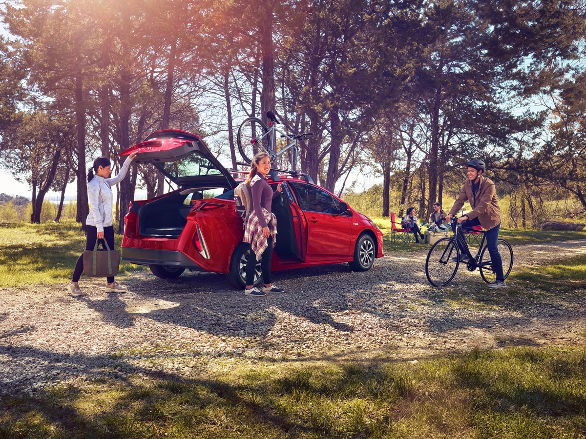 2021-Toyota-PriusPrime-Limited-Hatchback-L03.png red Toyota Prius hatchback at a park with driver and passengers on bikes nearby