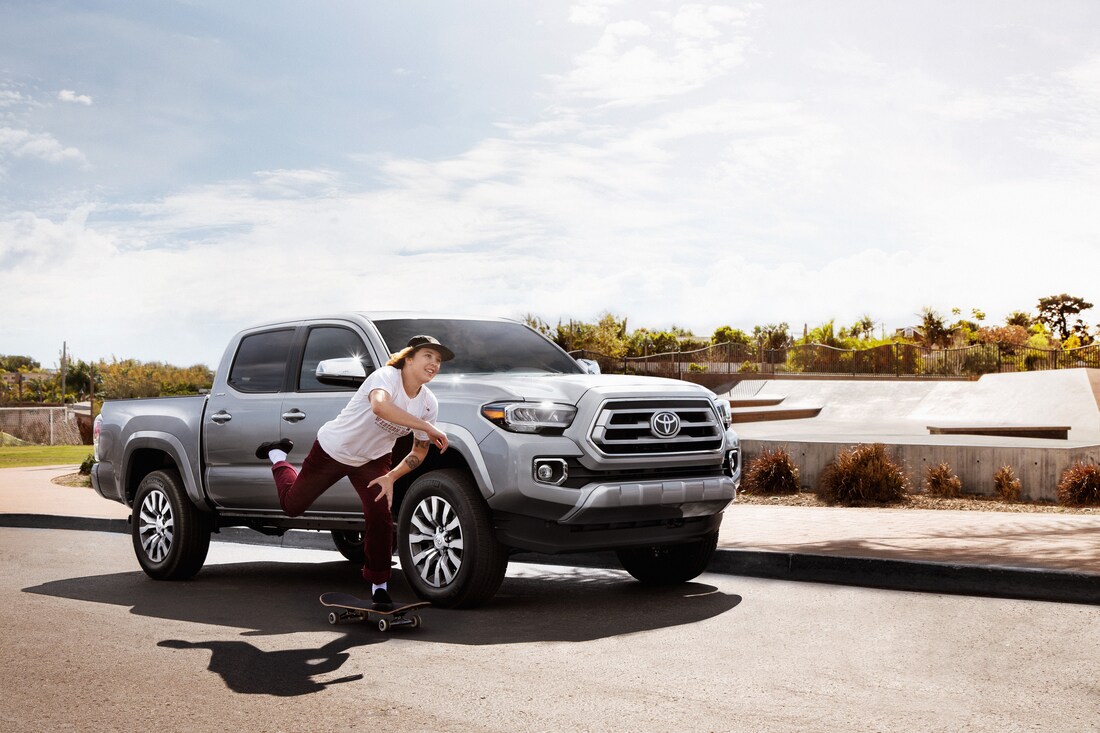 2022-Toyota-Tacoma-Limited-DoubleCab-Truck-L02.png silver Toyota Tacoma truck parked on the pavement with a skater riding by