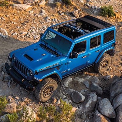 blue Jeep Wrangler Rubicon SUV bouldering over desert rocks