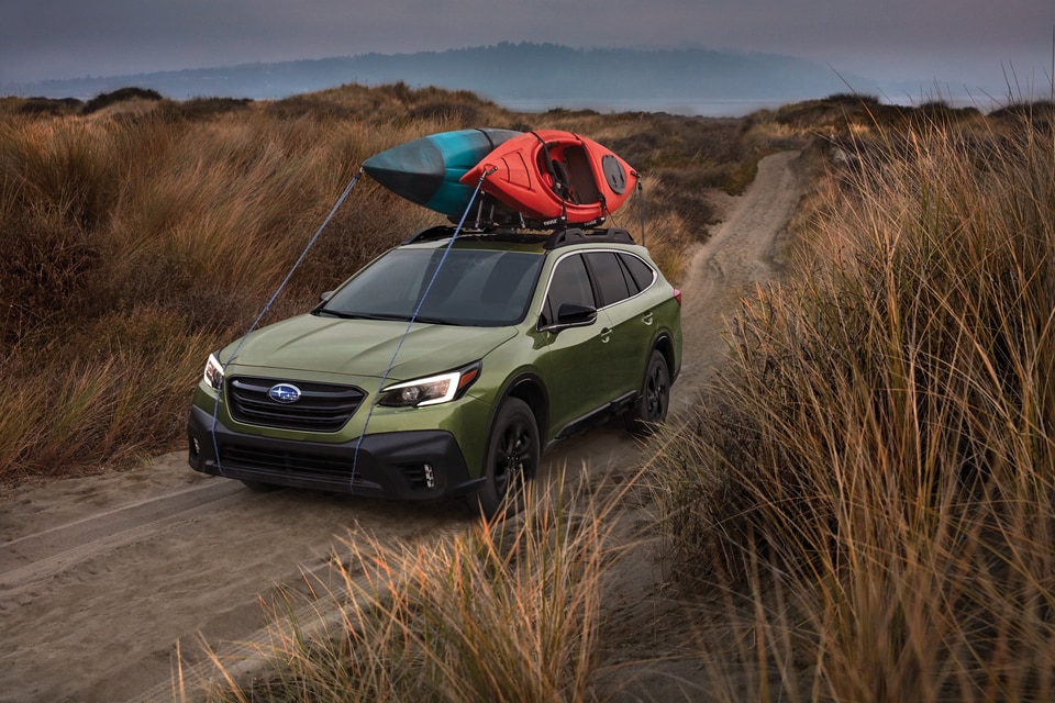 2020-Subaru-Outback-OnyxXT-SUV-L02.png green Subaru Outback SUV parked in a sandy beach field of tall grass, loaded with kayaks on the roof rack