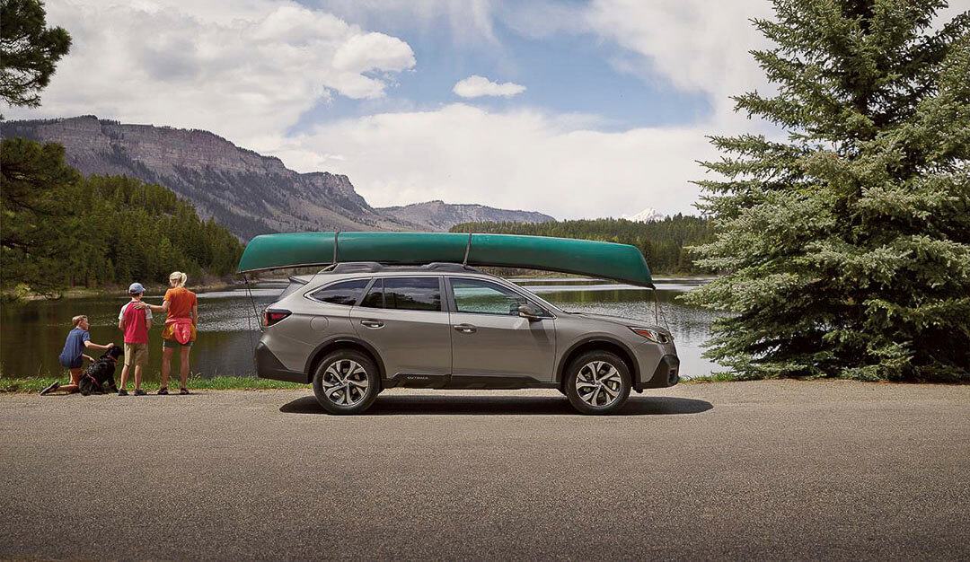 Vue latérale d'un VUS Subaru Outback 2022 avec une chaloupe attachée sur le toit au bord d'un lac