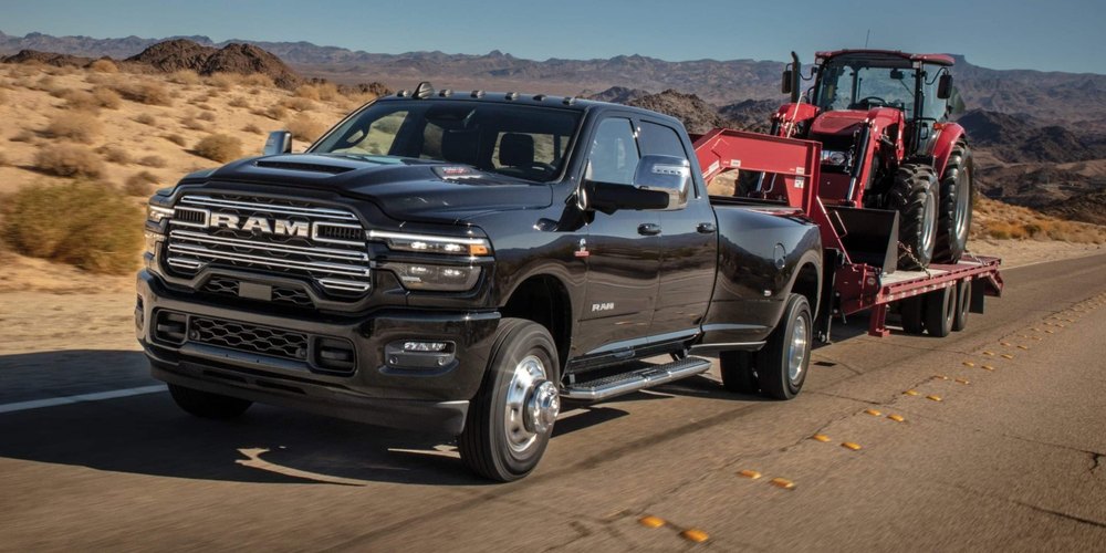 A black 2027 Ram 3500 dual-rear-wheel truck towing a tractor on a flatbed trailer
