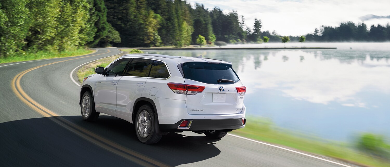 HLH19_LakeRoad_White.jpg Rearview of the 2019 Highlander Hybrid driving on a lakeside road