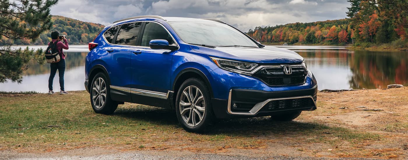 A blue 2022 Honda CR-V is shown next to a lake and a photographer.