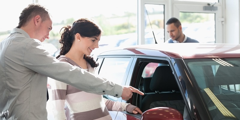 Car dealer pointing the interior of a car with a woman