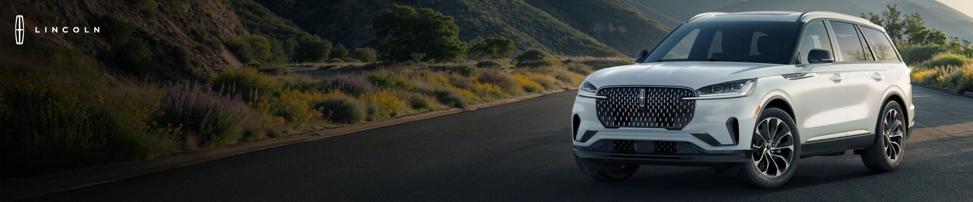 Three-quarter front view of a Lincoln Aviator Reserve in White parked on a scenic mountain road.