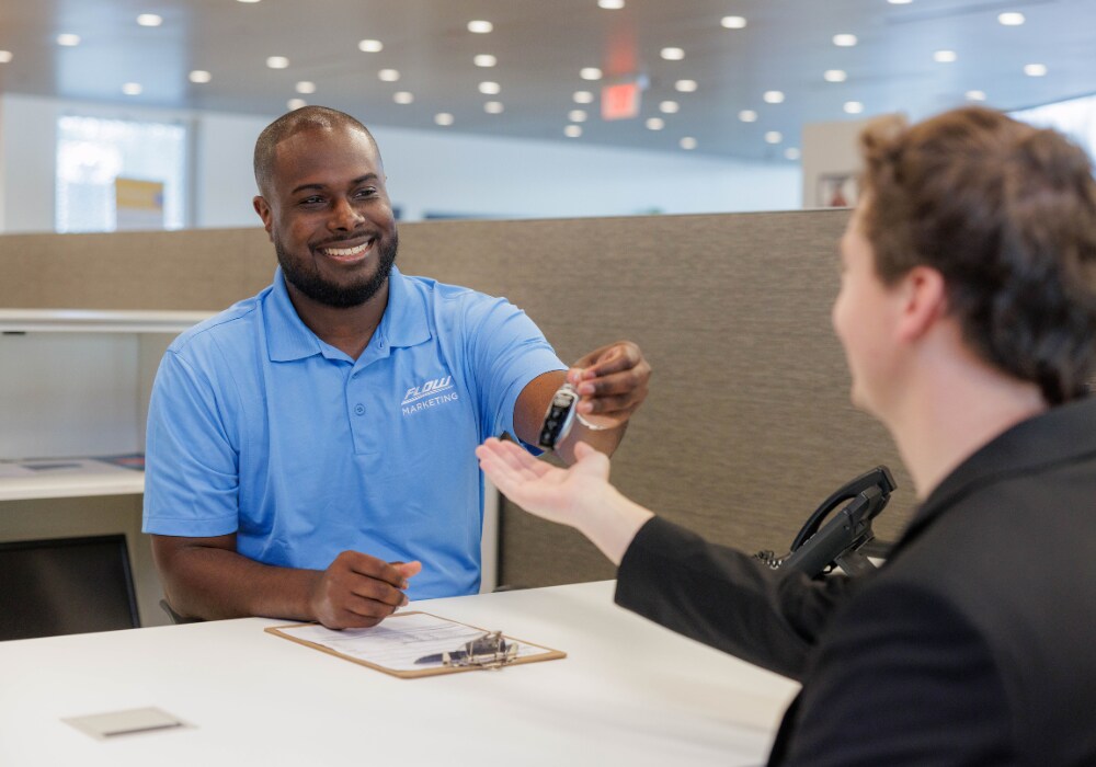 used-cars-winston-salem.png A Flow employee smiling and passing a car key to a customer across a desk inside a Flow dealership