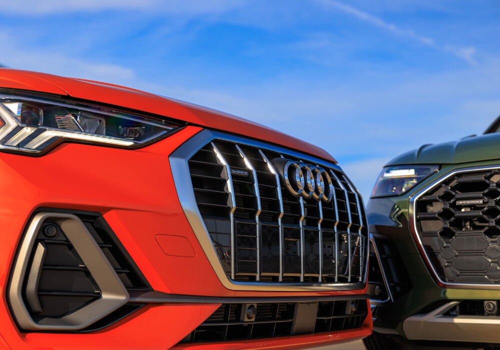 audi-electric-vehicles-charlottesville.png Close up photo of the grille of an orange 2024 Audi electric SUV. There is another green 2024 Audi SUV slightly out of frame