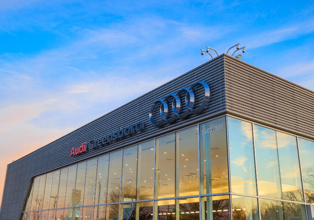 used-audi-cars-for-sale-greensboro.png Audi Greensboro dealership storefront with a blue sky in the background. The Audi logo appears on the front of the building next to the store name