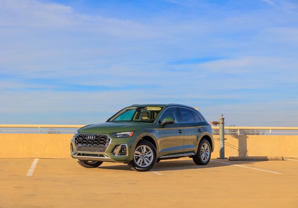 2024-audi-q5.png Green 2024 Audi Q5 parked on top of a parking garage with a blue sky in the background