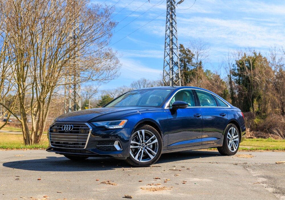 2024-audi-a6-winston-salem.png A blue 2021 Audi A6 sedan parked in a parking lot in Winston-Salem, NC. The car is facing the camera, showing its front. There are trees and a clear sky in the background.