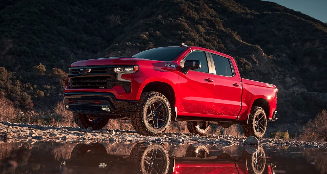 Red 2024 Chevrolet Silverado 1500 driving on a gravel road with mountains in the background