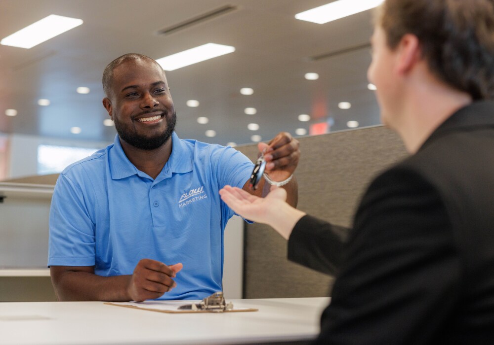 used-cars-fayetteville.png A Flow employee smiling and passing a car key to a customer inside the Flow Buick GMC dealership in Fayetteville