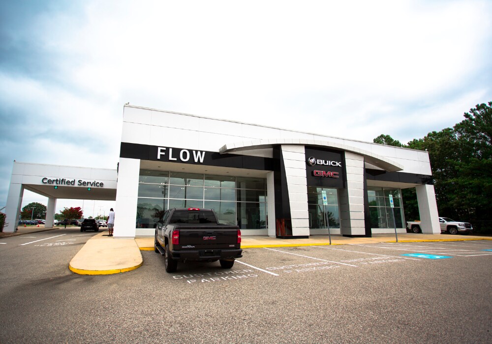 used-buick-for-sale.png Flow Buick GMC dealership storefront with a GMC trucks parked out front. There is a cloudy sky in the background