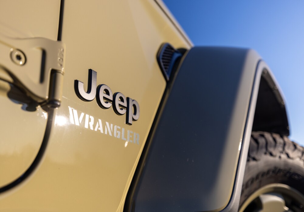 jeep-wrangler-hybrid-engine.png Jeep Wrangler logo attached to the side of a tan colored Jeep Wrangler