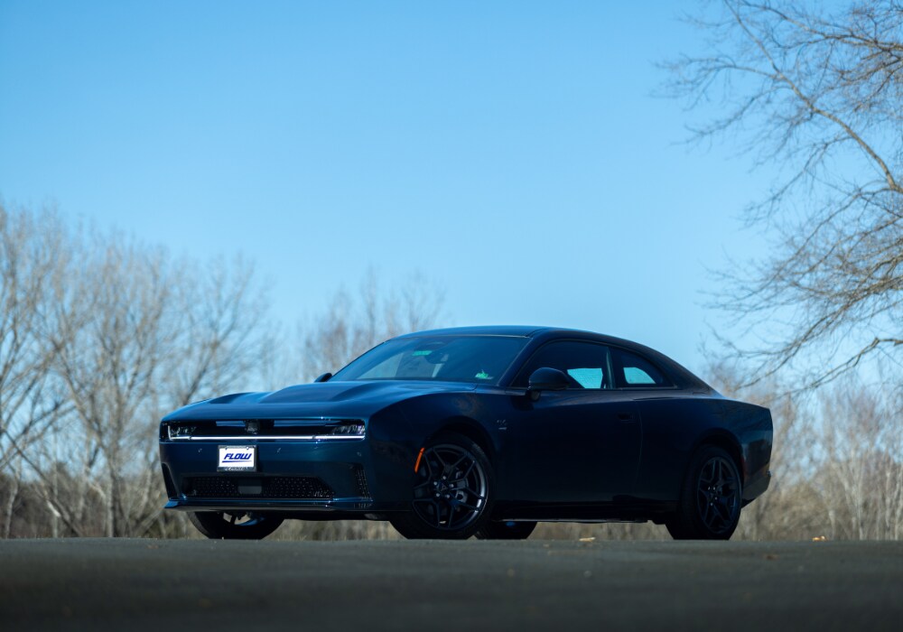 dodge-charger-for-sale-charlottesville-va.png Black 2025 Dodge Charger in a parking lot with a blue sky in the background. There is a Flow logo on the front license plate