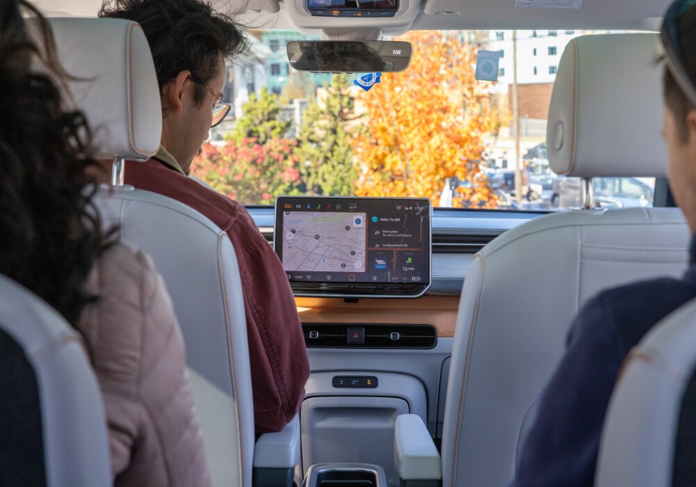 vw-id-buzz-interior.png The interior of a 2025 VW ID. Buzz. There is a map visible on the infotainment system and the seats are white. There are three people in the car, including one in the driver's seat