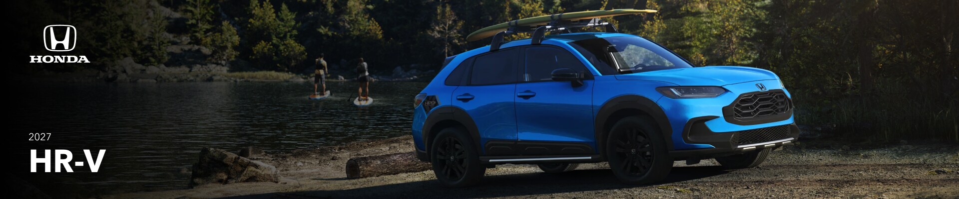 An exterior shot of a blue 2027 Honda HR-V with a surfboard o its roof rack parked on a forested waterfront.