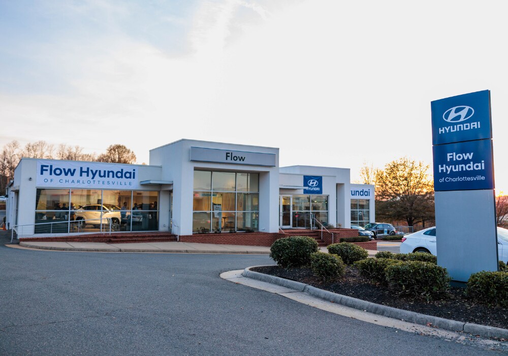 hyundai-dealership-serving-staunton-va.png Exterior shot of the Flow Hyundai of Charlottesville car dealership. There are cars parked outside the building and a sunset in the background