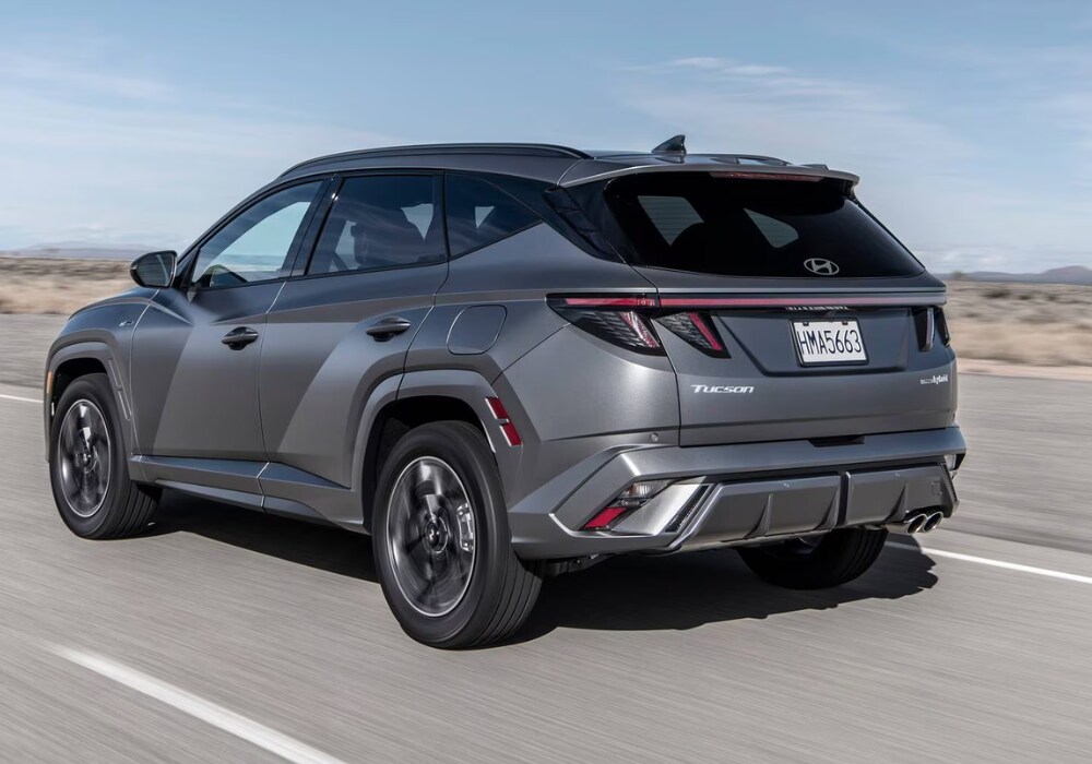 hyundai-tucson-specs.png 2025 Hyundai Tucson SUV driving down a road away from the camera. There is a blue sky in the background and the Hyundai logo is visible on the back of the car