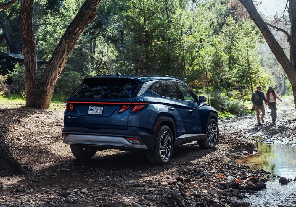 2024-hyundai-tucson-suv.png 2024 Hyundai Tucson paked in the woods. There is a man and woman walking toward the SUV