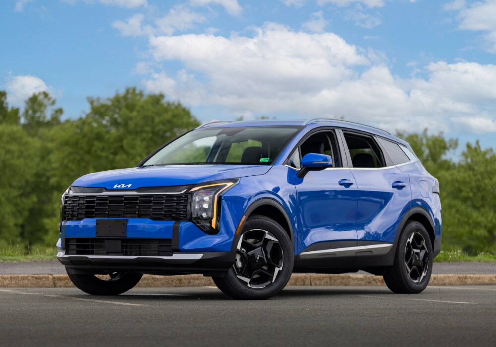 2025-kia-sportage-for-sale.png 2025 Kia Sportage for sale parked on a paved lot. The SUV is bright blue and there are trees in the background