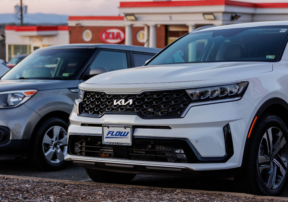 used-kia-for-sale.png Close up photo of a white Kia SUV for sale in Charlottesville. the Flow Kia of Charlottesville dealership is visible in the background
