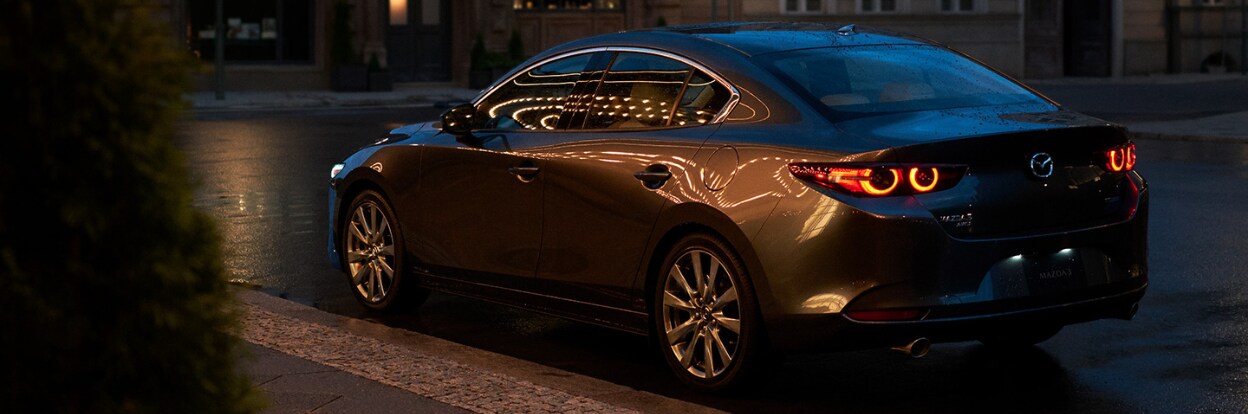 mazda3-trim-breakdown.png Mazda3 sedan parked on a city street. There are city lights being reflected on the body of the car