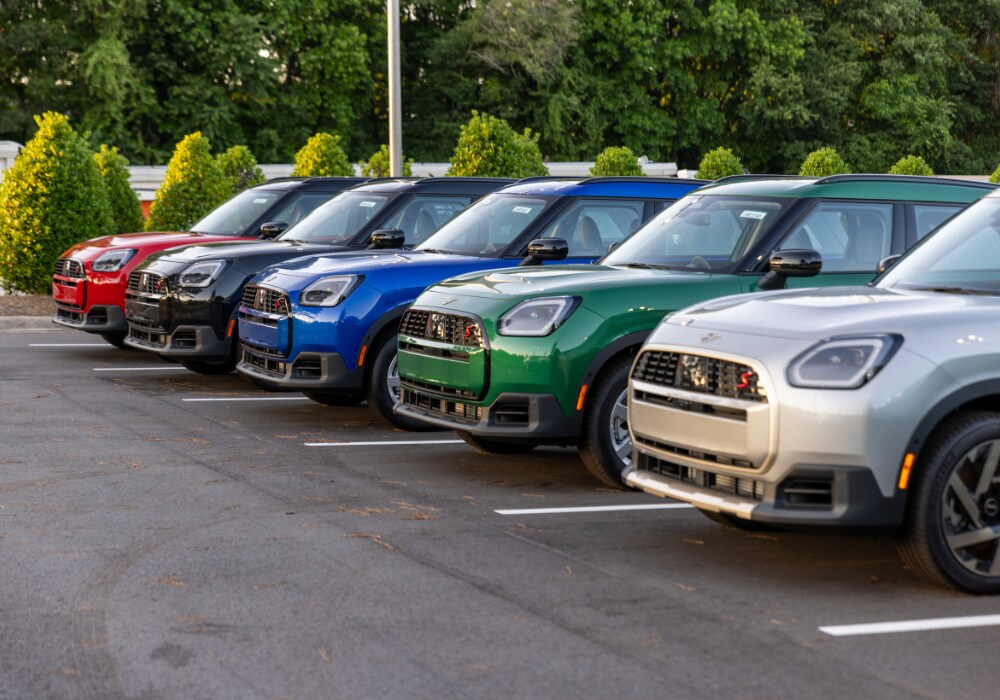 used-cars-in-raleigh-nc.png Lineup of MINI cars for sale at Flow MINI of Raleigh. They are parked in a row on a paved lot and there are trees in the background