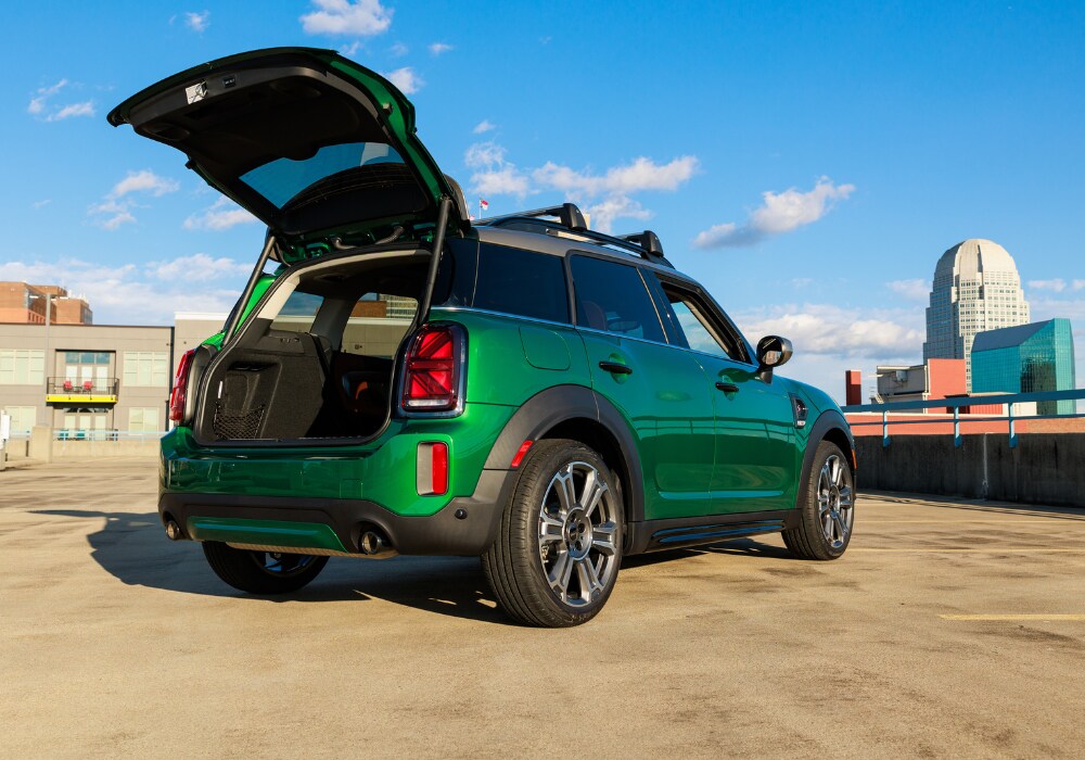 mini-cooper-countryman-near-me.png MINI Countryman with its trunk open. The compact SUV is green and there are buildings in the background of the photo