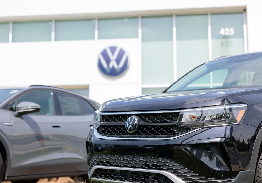volkswagen-certified-pre-owned-cars-winston-salem.png Close up of the front of a Volkswagen SUV with a Volkswagen dealership storefront out of focus in the background