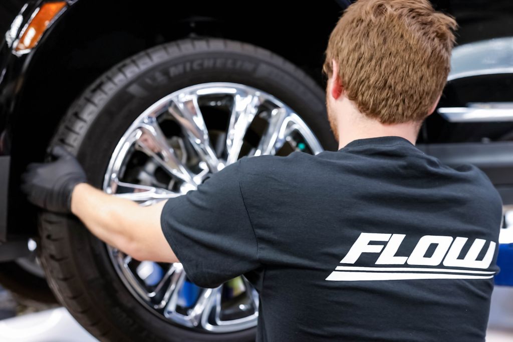 nissan-service-fayetteville-lumberton-nc.jpg Automotive service technician adjusts tire on a vehicle, with back of shirt displaying a Flow Automotive logo - at Nissan Fayetteville