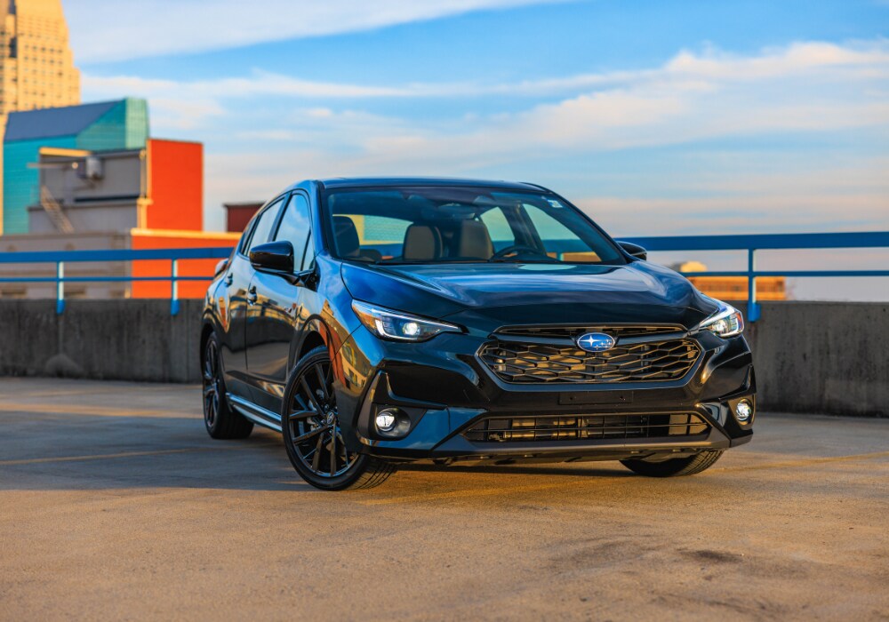 new-subaru-cars-for-sale-winston-salem.png Black Subaru car for sale parked on top of a parking deck with the downtown Winston-Salem skyline in the background