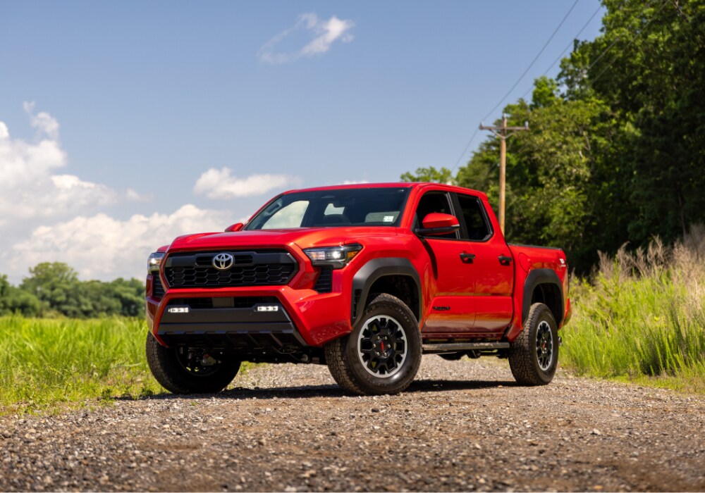 2025-toyota-tacoma-for-sale.png Red 2025 Toyota Tacoma truck parked on a gravel road with trees in the background