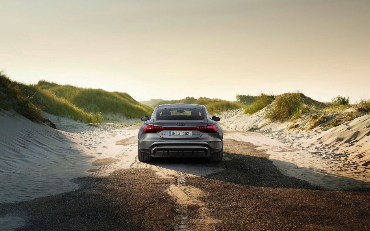 vue arrière d'une Audi E-tron GT 2023 sur une route bordée de dunes de sable et d'herbe