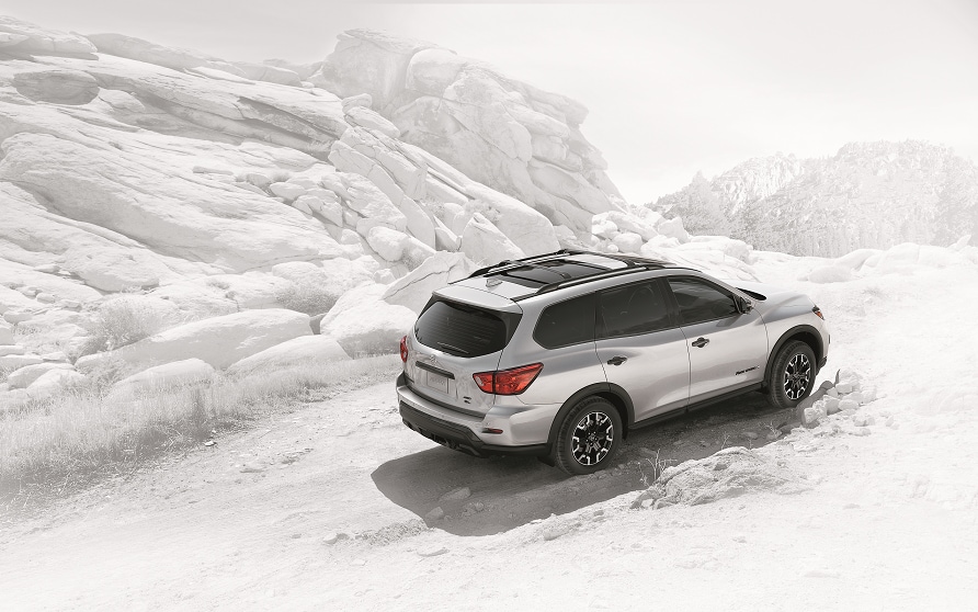 Silver Nissan Pathfinder on a snowy road. Pathfinder features a roof rack