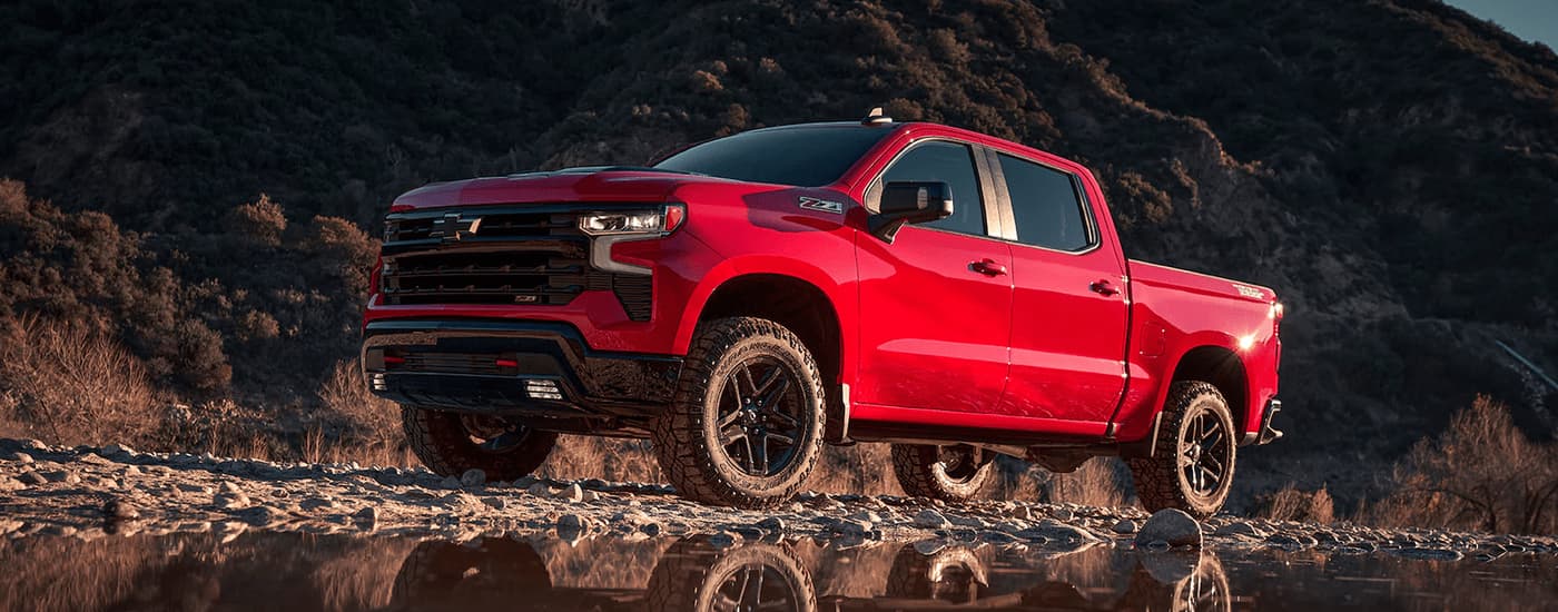2023 Chevy Silverado Z71 - Red Rocks.jpg A red 2023 Chevy Silverado Z71 is shown parked on rocks next to a small body of water.