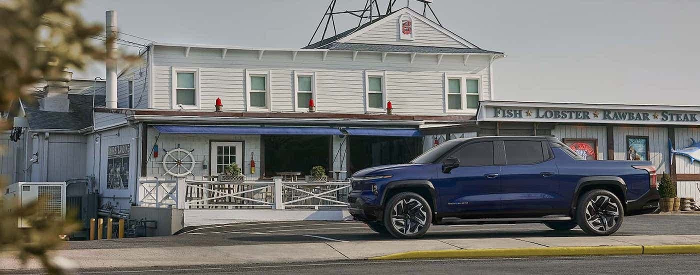2024 Chevy Silverado EV - Seafood.jpg A blue 2024 Chevy Silverado EV is shown from the side outside of a seafood restaurant.