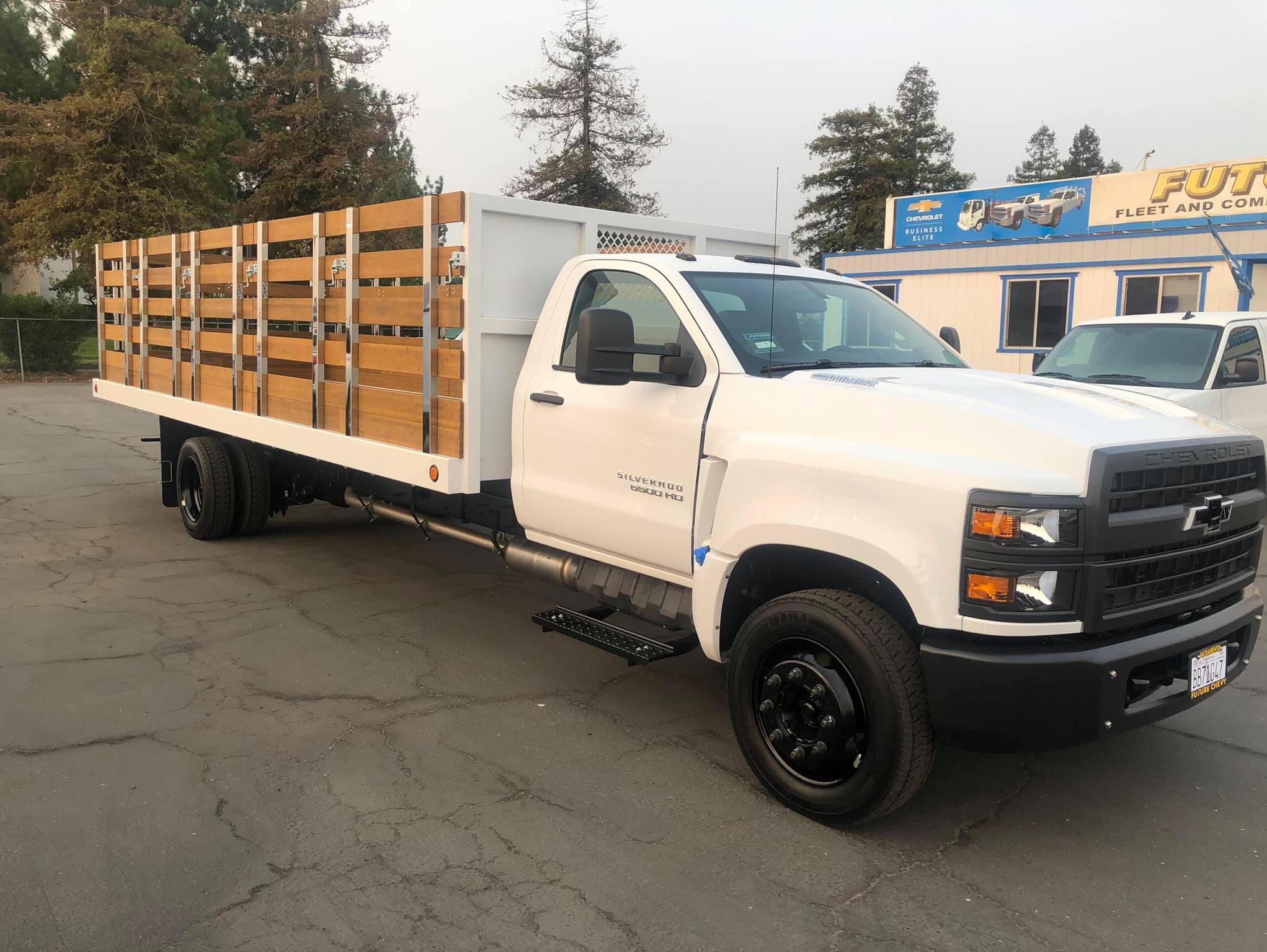 White Chevy Silverado 6500HD with 22 foot Royal Flat Bed with wooden stakes, side view
