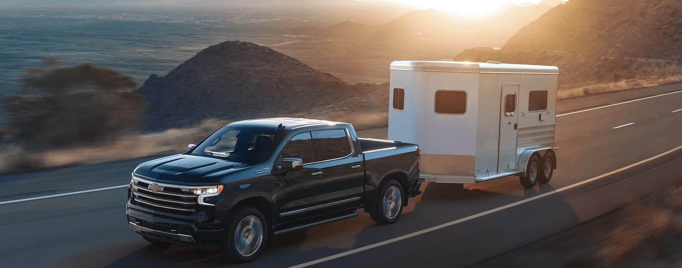 2023 Chevy Silverado 1500 High Country - Towing.jpg A black 2023 Chevy Silverado 1500 High Country is shown towing a trailer on a highway.