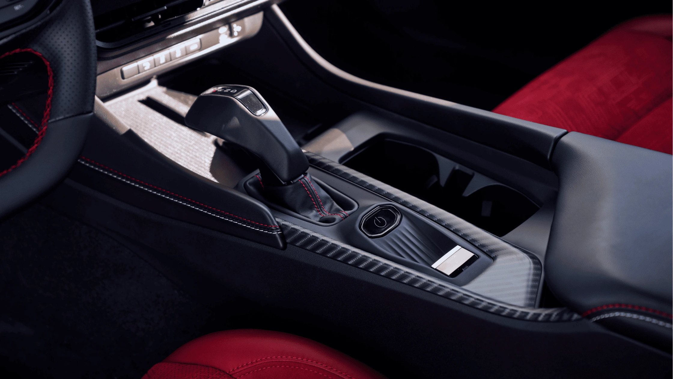 2024 Dodge Charger Daytona - Cutting-Edge Safety and Driver Assistance Close-up of the gear shift console in a modern sports car, featuring a sleek black finish, red contrast stitching, and carbon fiber accents, highlighting its premium interior design.