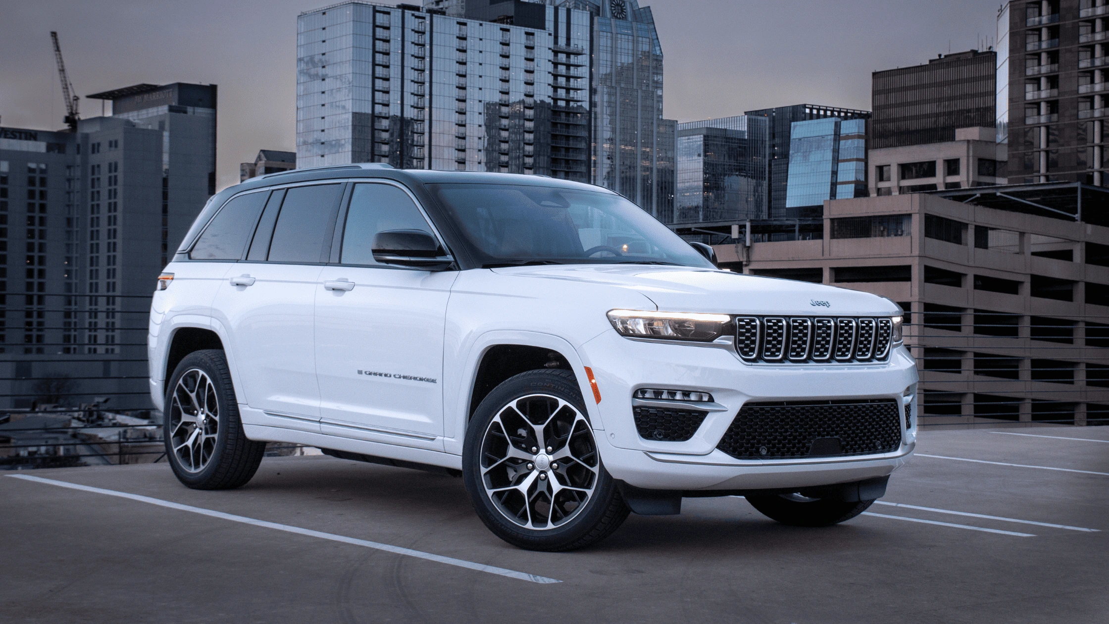 2025 Jeep® Grand Cherokee 4xe in Fort Myers, FL White 2025 Jeep Grand Cherokee 4xe parked in a Fort Myers rooftop cityscape